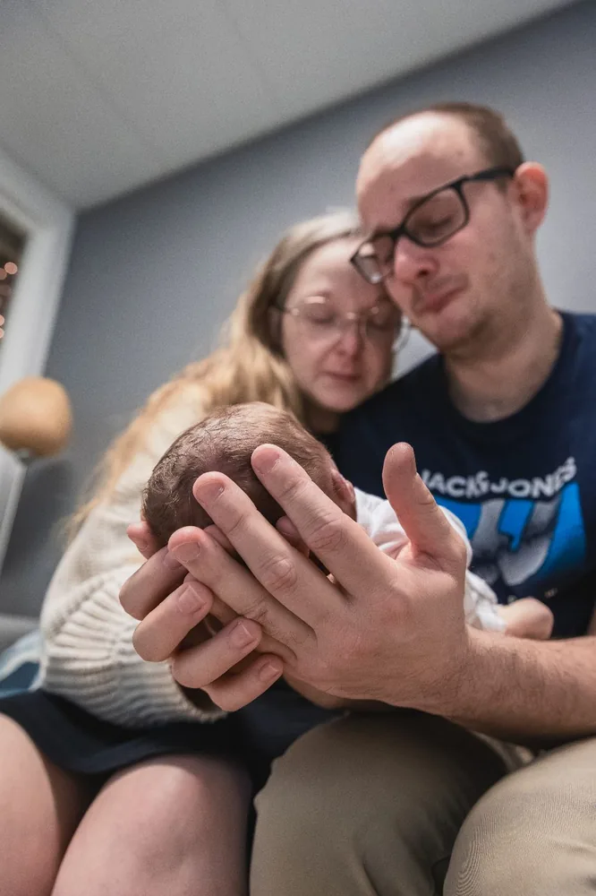 De handen van mama en papa rond Senne.