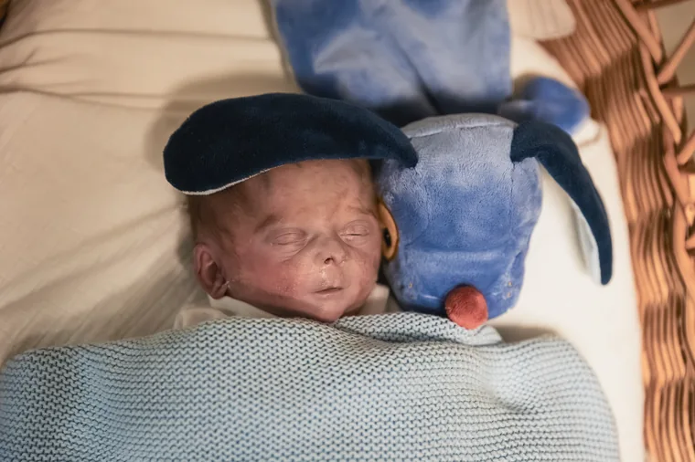 Senne slapend in de rieten wieg, met zijn blauwe knuffelhond naast zich.